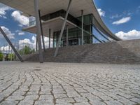 a person on a bike walking through a stone building entrance, in front of an enormous glass wall and stairs