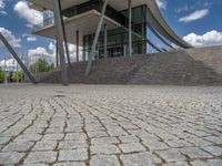 a person on a bike walking through a stone building entrance, in front of an enormous glass wall and stairs