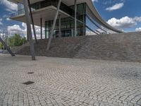 a person on a bike walking through a stone building entrance, in front of an enormous glass wall and stairs