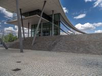 a person on a bike walking through a stone building entrance, in front of an enormous glass wall and stairs