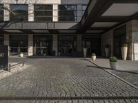 a building with large windows near the sidewalk with cobblestone walkways and stone wall