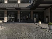 a building with large windows near the sidewalk with cobblestone walkways and stone wall