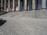 a boy sitting on the steps of a museum near to stone statues and columns, watching something going up