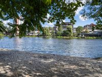 the view from a bench at the river bank near the park benches and buildings in the distance