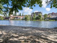 the view from a bench at the river bank near the park benches and buildings in the distance