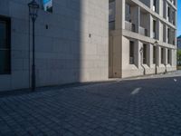 two people walking down an empty city street in an alley area with tall buildings in the background