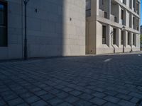 two people walking down an empty city street in an alley area with tall buildings in the background