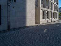 two people walking down an empty city street in an alley area with tall buildings in the background