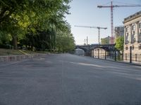 an empty street next to the buildings and some trees and a street light and some cranes