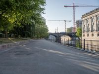 an empty street next to the buildings and some trees and a street light and some cranes