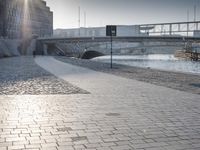 there is a street sign by the river and people walking in the city streets on cobblestone pavement