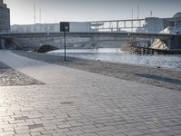 there is a street sign by the river and people walking in the city streets on cobblestone pavement