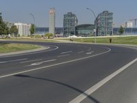 the street with two cars is empty in front of some city buildings by water in a sunny day