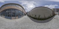 two spherical photographs are shown in the middle of a walkway, with a circular object on the right and some buildings on the left