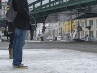 a person on a city street with an umbrella in the snow with a bridge above them