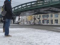 a person on a city street with an umbrella in the snow with a bridge above them