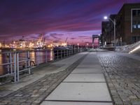 a walkway next to the water at dusk with a red sky in the background that seems to be on fire