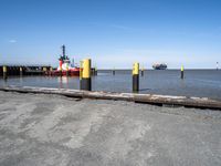 there is a ship in the water, at the dock, with yellow poles on the ground