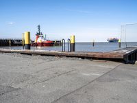 there is a ship in the water, at the dock, with yellow poles on the ground