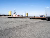 there is a ship in the water, at the dock, with yellow poles on the ground