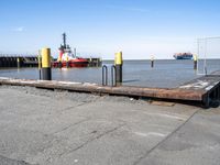 there is a ship in the water, at the dock, with yellow poles on the ground