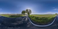 an intersection shows a road lined with white strips of grass and a grassy field is seen in this 360 - vr shot