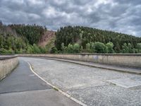 concrete walkway with trees and fenced in area on opposite sides of the road and one side of the road