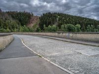 concrete walkway with trees and fenced in area on opposite sides of the road and one side of the road