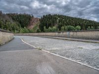 concrete walkway with trees and fenced in area on opposite sides of the road and one side of the road