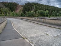 concrete walkway with trees and fenced in area on opposite sides of the road and one side of the road