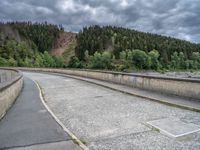 concrete walkway with trees and fenced in area on opposite sides of the road and one side of the road