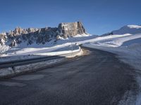 a snow covered hill sits in the distance on a road that is blocked by large snow piles