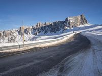 a snow covered hill sits in the distance on a road that is blocked by large snow piles