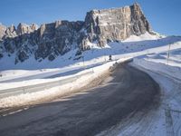 a snow covered hill sits in the distance on a road that is blocked by large snow piles