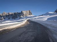 a snow covered hill sits in the distance on a road that is blocked by large snow piles