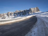 a snow covered hill sits in the distance on a road that is blocked by large snow piles