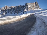 a snow covered hill sits in the distance on a road that is blocked by large snow piles