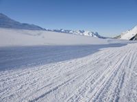 a skier goes down a snowy ski trail towards the mountains in the distance is snow covered hills