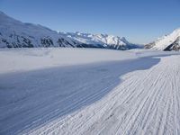 a skier goes down a snowy ski trail towards the mountains in the distance is snow covered hills