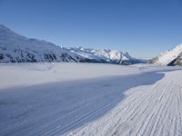 a skier goes down a snowy ski trail towards the mountains in the distance is snow covered hills