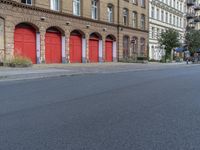 a city street in front of buildings with red doors and no curb on them is an empty area with trees