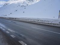 a road in the middle of the mountains covered in snow and ice with a car parked at the side