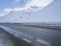 a road in the middle of the mountains covered in snow and ice with a car parked at the side