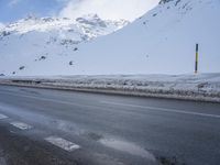 a road in the middle of the mountains covered in snow and ice with a car parked at the side