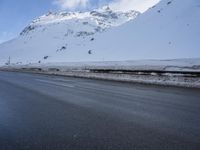 a road in the middle of the mountains covered in snow and ice with a car parked at the side
