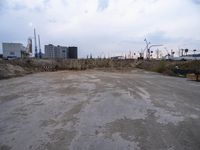 a empty parking lot in front of construction cranes and large buildings at dusk in an industrial area