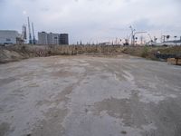 a empty parking lot in front of construction cranes and large buildings at dusk in an industrial area