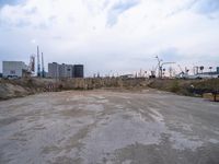 a empty parking lot in front of construction cranes and large buildings at dusk in an industrial area