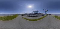 a fish eye lens view of the entrance to a beach park and parking lot, with trees and bushes at the shoreline