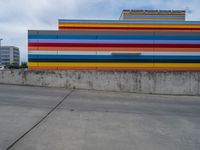 an empty parking lot painted brightly stripes on the wall of the building and sky as well as stones